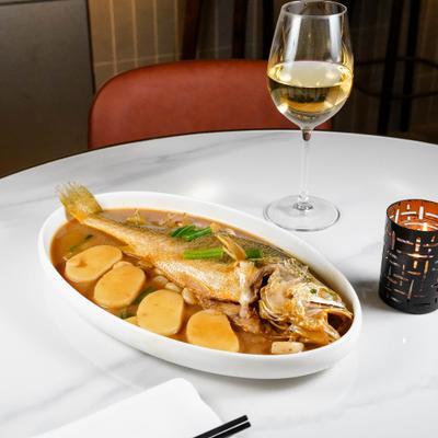 Steamed yellow croaker in ginger broth with potatoes, alongside a glass of wine.