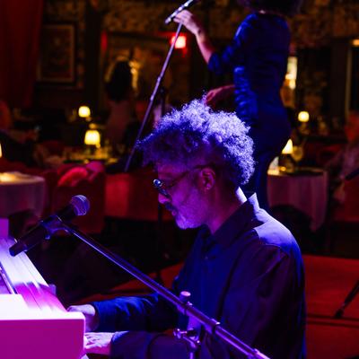 Pianist playing the piano with singer partially visible in the background.