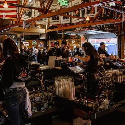 Busy bar area viewed from behind the bar, with bartenders helping customers.