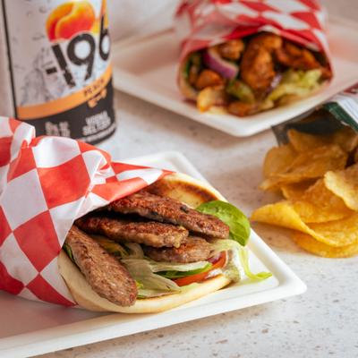 Gyro Pita sandwick on the table with chips and a drink.