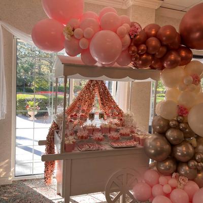 A baby shower candy cart with decorations,  pink, gold, white, and silver balloons