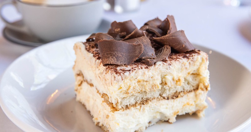 A slice of tiramisu topped with chocolate shavings sits on a white plate
