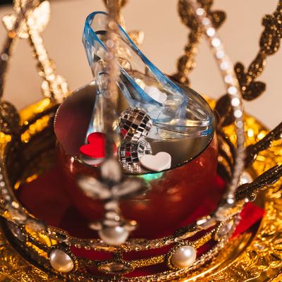 Golden ornate crown holds a glass slipper with small red and white heart cutouts.