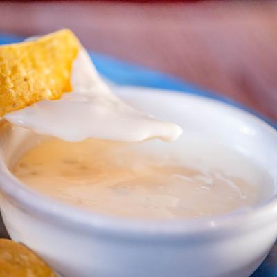 Creamy white queso dip with tortilla chip.