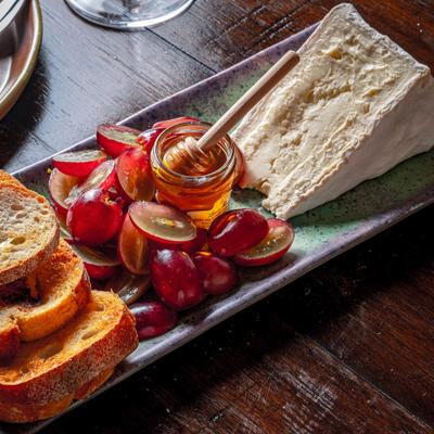 Burgundy board with grapes honey cheese and bread.