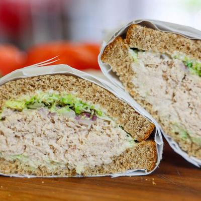 A tuna sandwich is cut in half, revealing layers of tuna salad and lettuce on whole-grain bread.