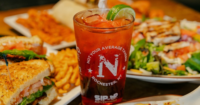 Cocktail in a branded pint glass, garnished with a slice of lime and served beside food