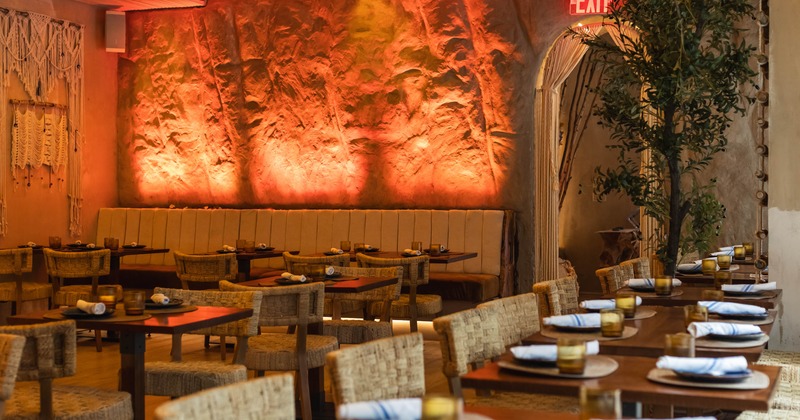 A warmly lit interior with textured walls, wicker chairs and wooden tables