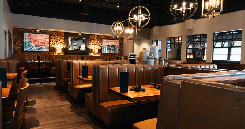 Interior of a restaurant with brown leather booths, wooden tables, and warm chandeliers