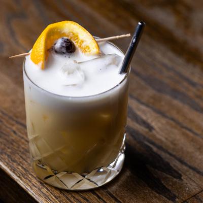 Whiskey Sour cocktail with cherry and orange garnish.