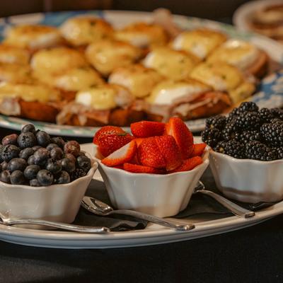 Bowls of blueberries, strawberries, and blackberries with Eggs Benedict platter in the background.