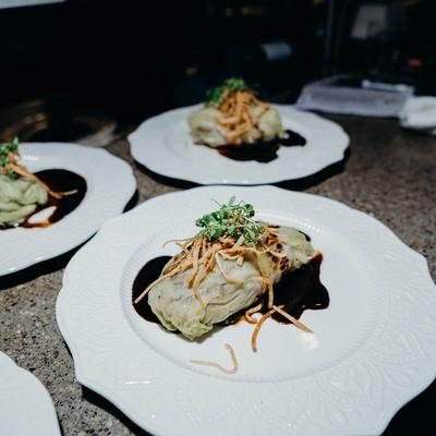 Three plates of cabbage rolls drizzled with sauce, topped with crispy onions and herbs.