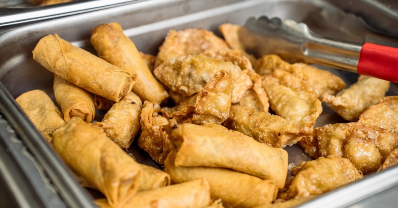 A metal buffet tray filled with crispy deep-fried spring rolls and dumplings