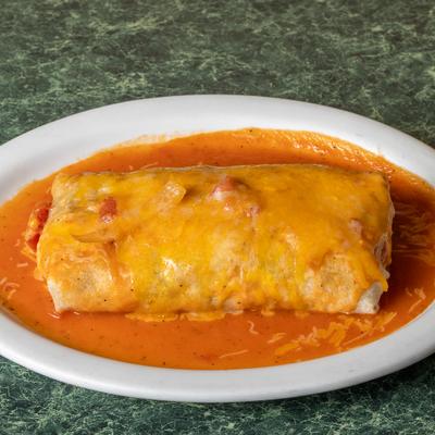 Wet burrito topped with melted cheese and served in a red sauce on a white plate.