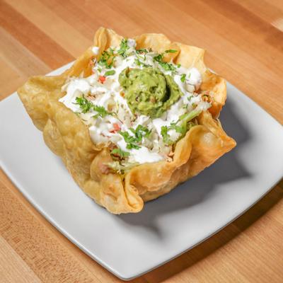 Taco salad in a crispy tortilla bowl with guacamole and sour cream.