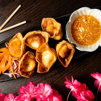 Crab Rangoon with dipping sauce and carrot garnish.