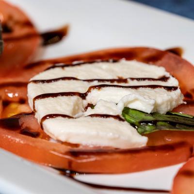 Caprese salad featuring tomato topped with mozzarela, basil and balsamic glaze.