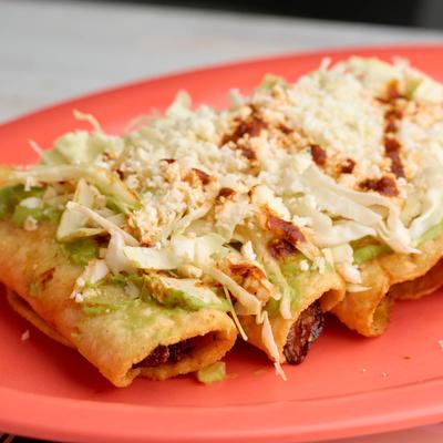 Taquitos, topped with guacamole salsa, cabbage, cheese, and red salsa.