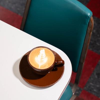 A latte in a brown cup on a white counter, a retro teal chair is visible.