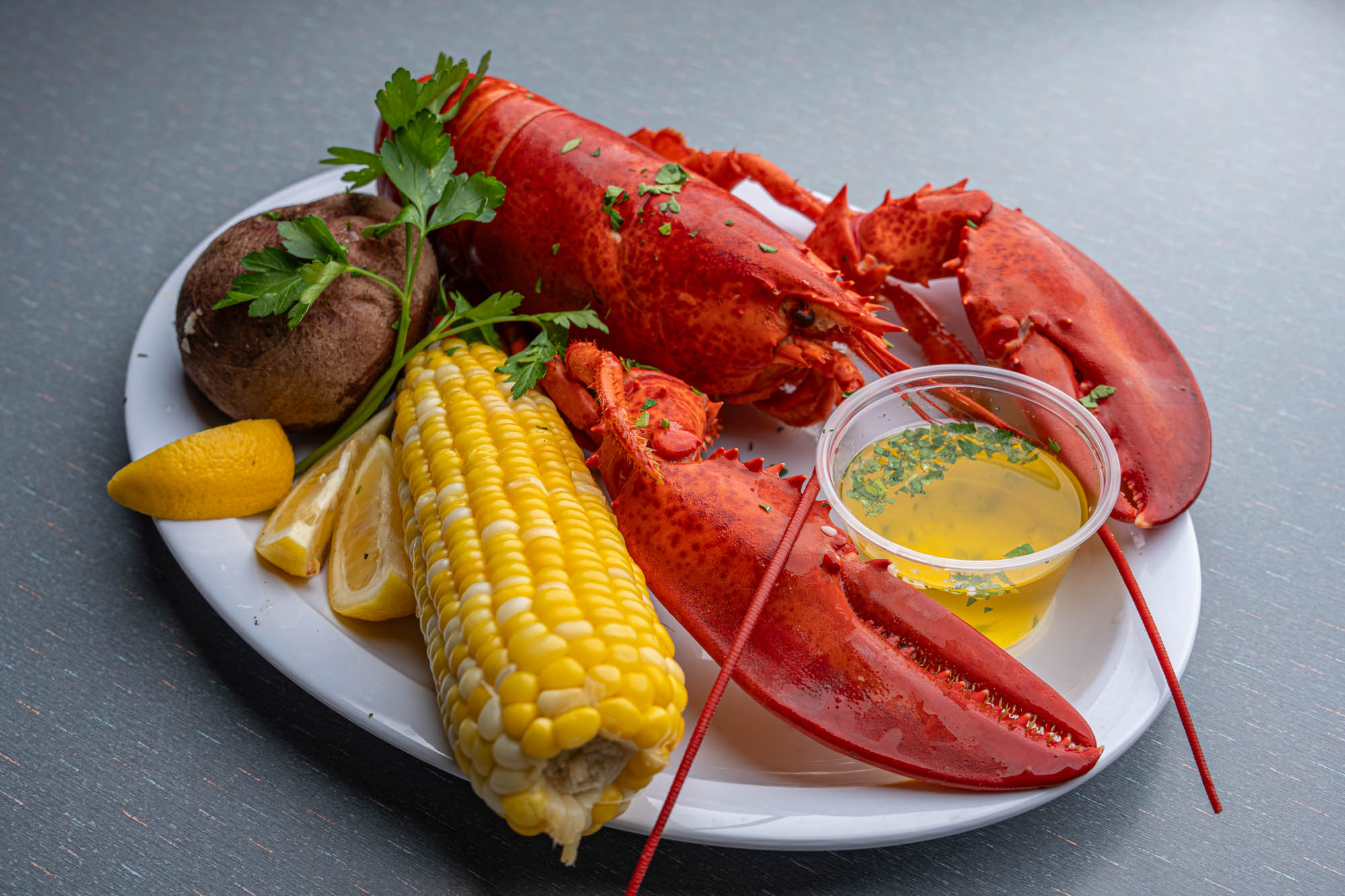 Lobster with a side of corn on the cob, baked potato, and a cup of drawn butter