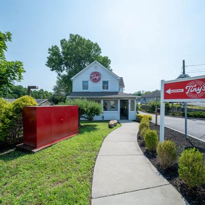 Concrete walkway leading toward a restaurant building with a red sign near a roadside.