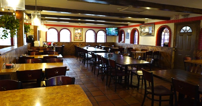 A cozy interior with rows of wooden tables and chairs, arched windows and warm lighting