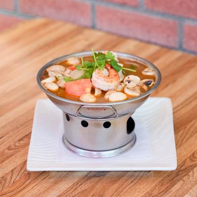 Tom Yum soup served in a traditional Thai hot pot on a square white plate.
