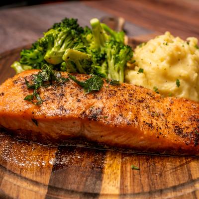 Pan-seared salmon served alongside mashed potatoes and broccoli on a wooden board.