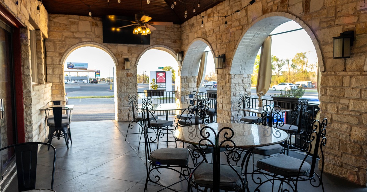 Covered outdoor seating area with stone walls, arched openings, ornate chairs and tables