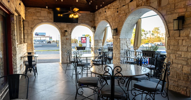 Covered outdoor seating area with stone walls, arched openings, ornate chairs and tables