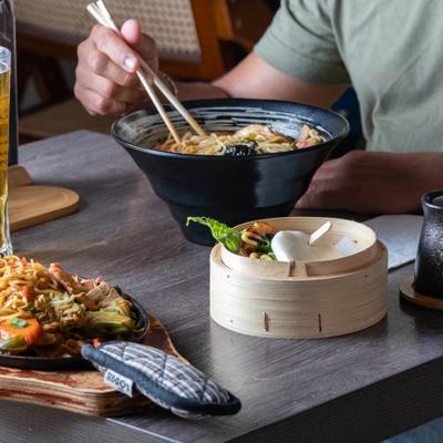 Person eating ramen beside dumplings and noodles.