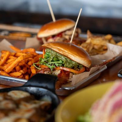 A close-up shot displays burgers, sweet potato fries, and side dishes.