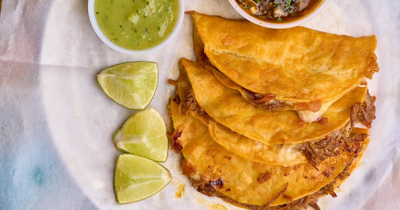 Birria tacos, served with lime, broth, and guacamole salsa