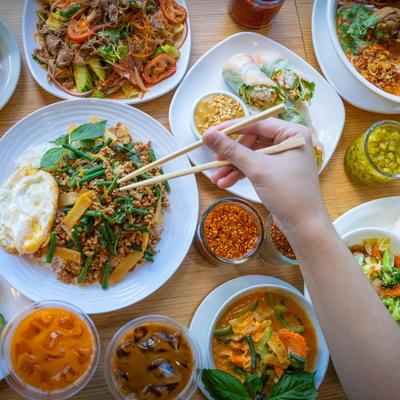 Assortment of dishes on a table, a person takes food with chopsticks, top view.