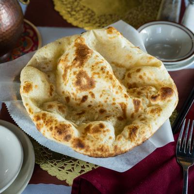 Naan on parchment paper, set on a decorative table with cutlery, a copper pot, and a red menu.