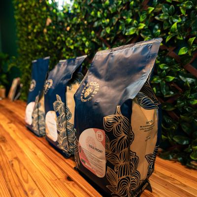 Three bags of coffee on a wooden table against a lush green backdrop.