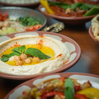 A plate of creamy hummus, nearby, a green dip and various dishes.