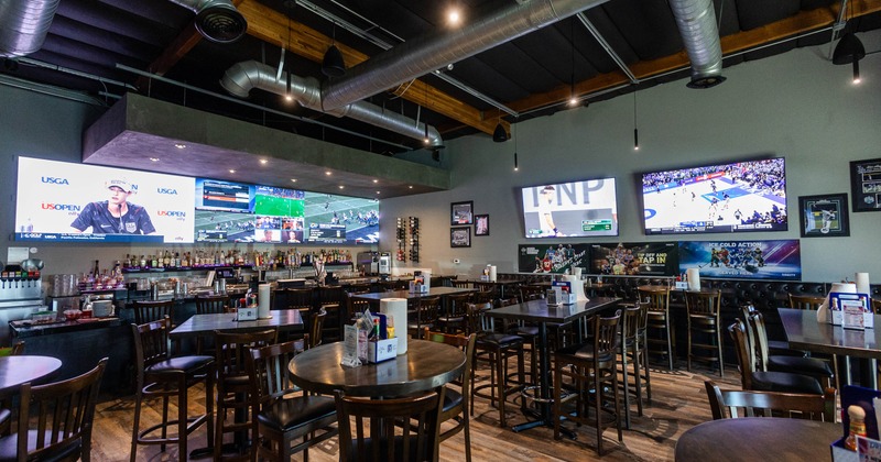 A modern sports bar with high ceilings, wooden tables, and chairs