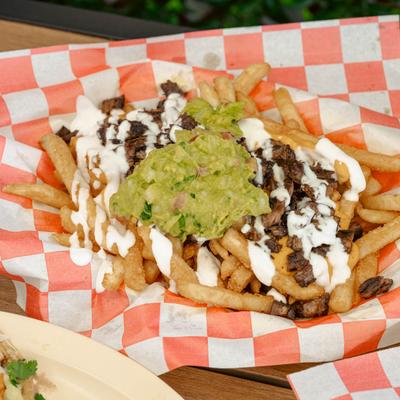 Asada Fries topped with guacamole and drizzled with crema.