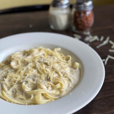 Fettuccini alfredo pasta in a white bowl with cheese on top.