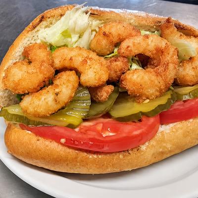 A shrimp sandwich with lettuce, tomato and pickles on a roll..