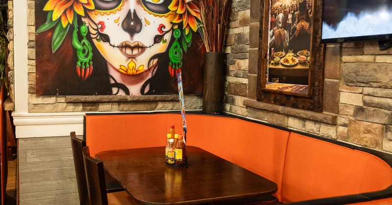 Restaurant dining area with a Day of the Dead mural and orange cushioned booth