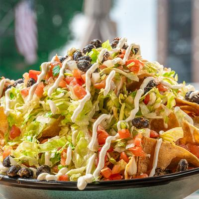 Loaded nachos topped with lettuce, tomatoes, and sauce.