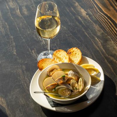 Bowl of clams with lemon wedges and toast served with a glass of wine.