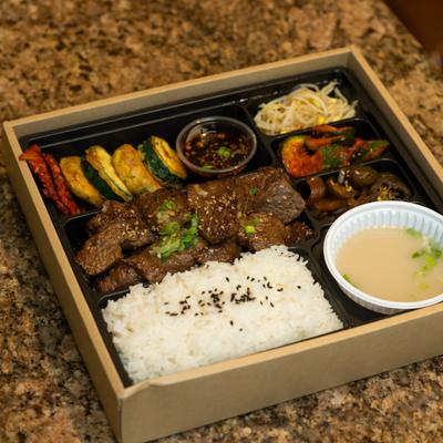 Korean lunch box with beef, rice, vegetables, and sauces.