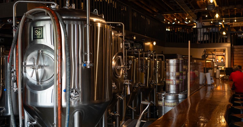 Large stainless steel brewing tanks beside a wooden bar inside a brewery
