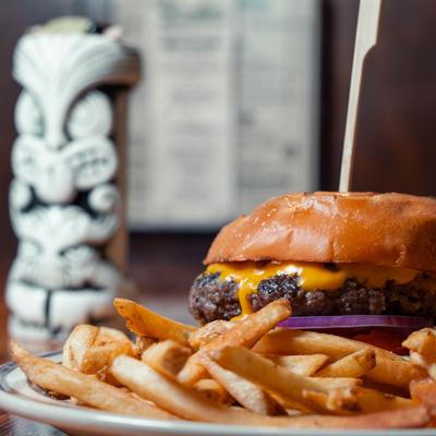 Longhorn burger with fries on the plate, a tiki drink is in the blurred background.