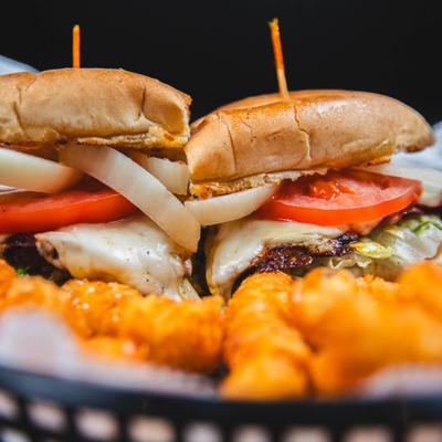 Chicken sandwich sliced in half and served with tater tots, close-up.