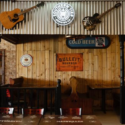 Interior featuring rustic wooden walls decorated with hung guitars and a neon sign.