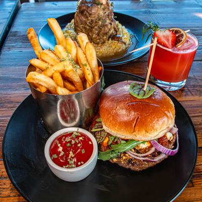 Lamb burger with fries and ketchup accompanied by a red cocktail and